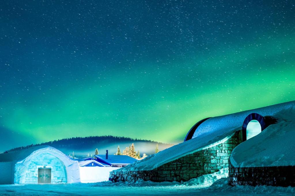 Snow resort at night with an aurora, a lit igloo and cabins