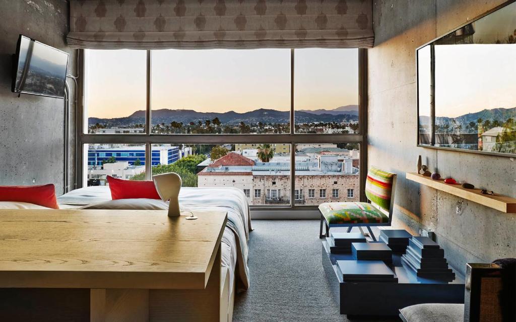 Hotel room with a concrete wall and a wide window onto a city at dusk
