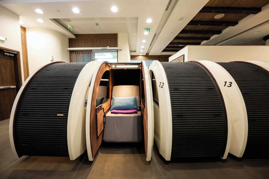 Row of airport sleeping pods, one open with a blue pillow